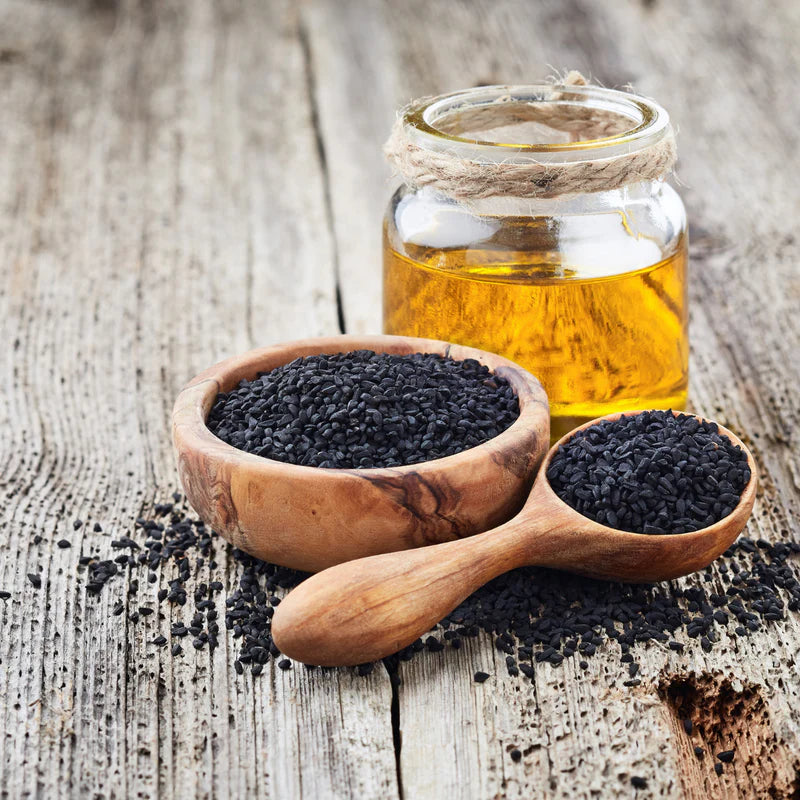 Black seeds in a wooden bowl and spoon with a jar of oil on a rustic wooden surface