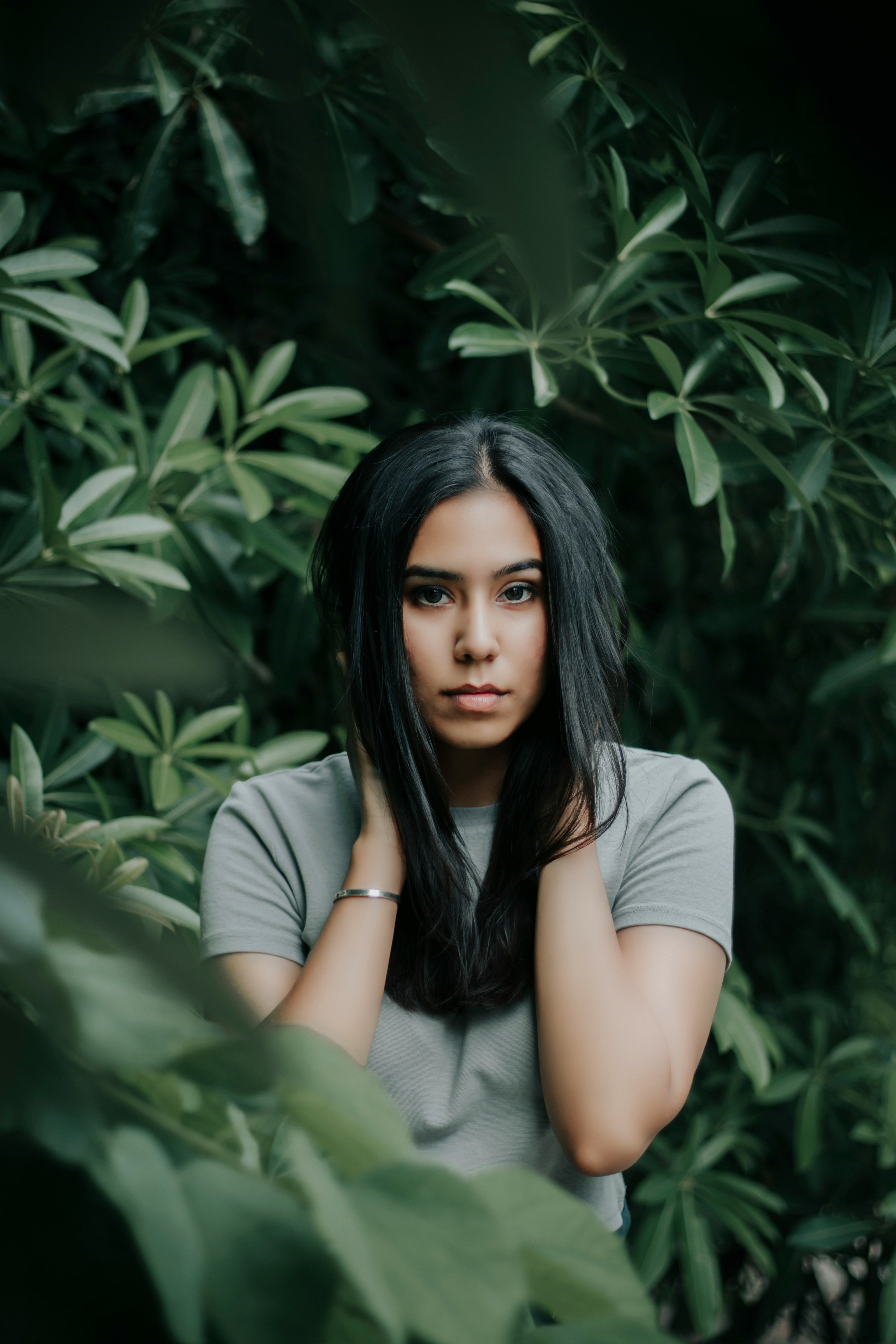 Woman with long dark hair sitting among green foliage